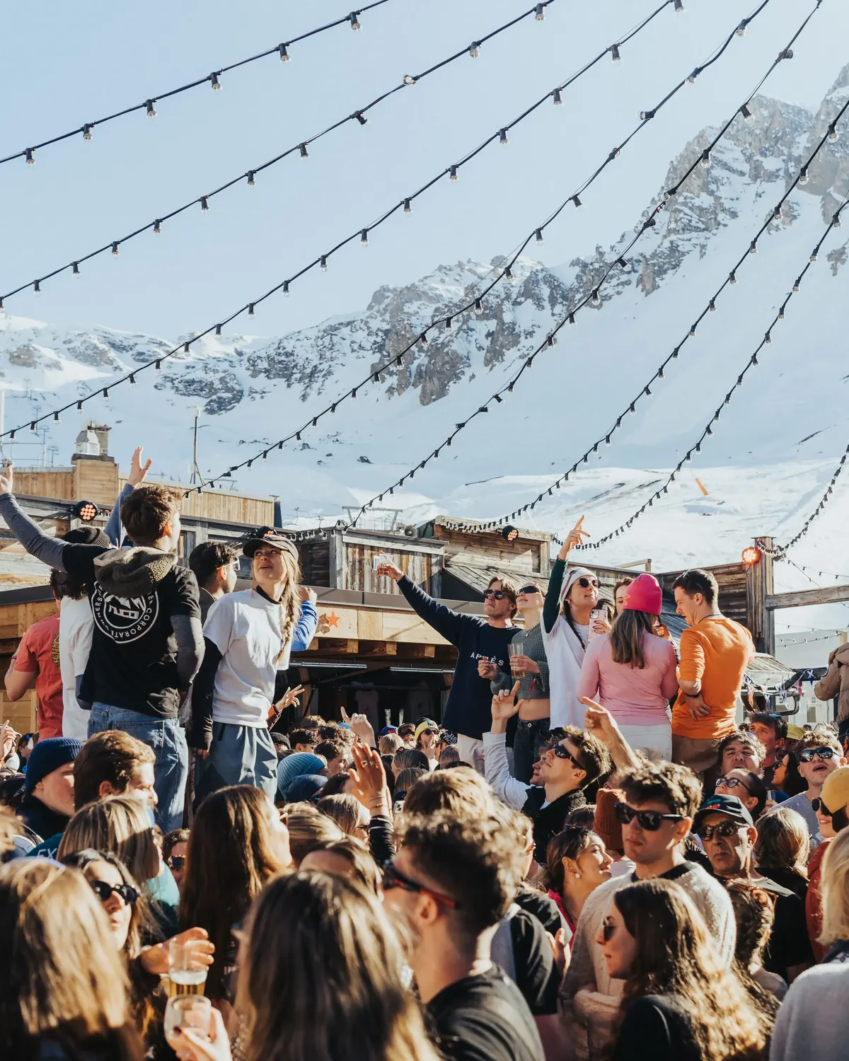Packed apres-ski bar under festoon lights with the mountains behind