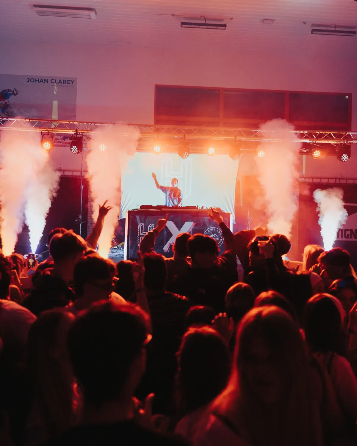 Crowd at an indoor party with the DJ booth lit red behind them