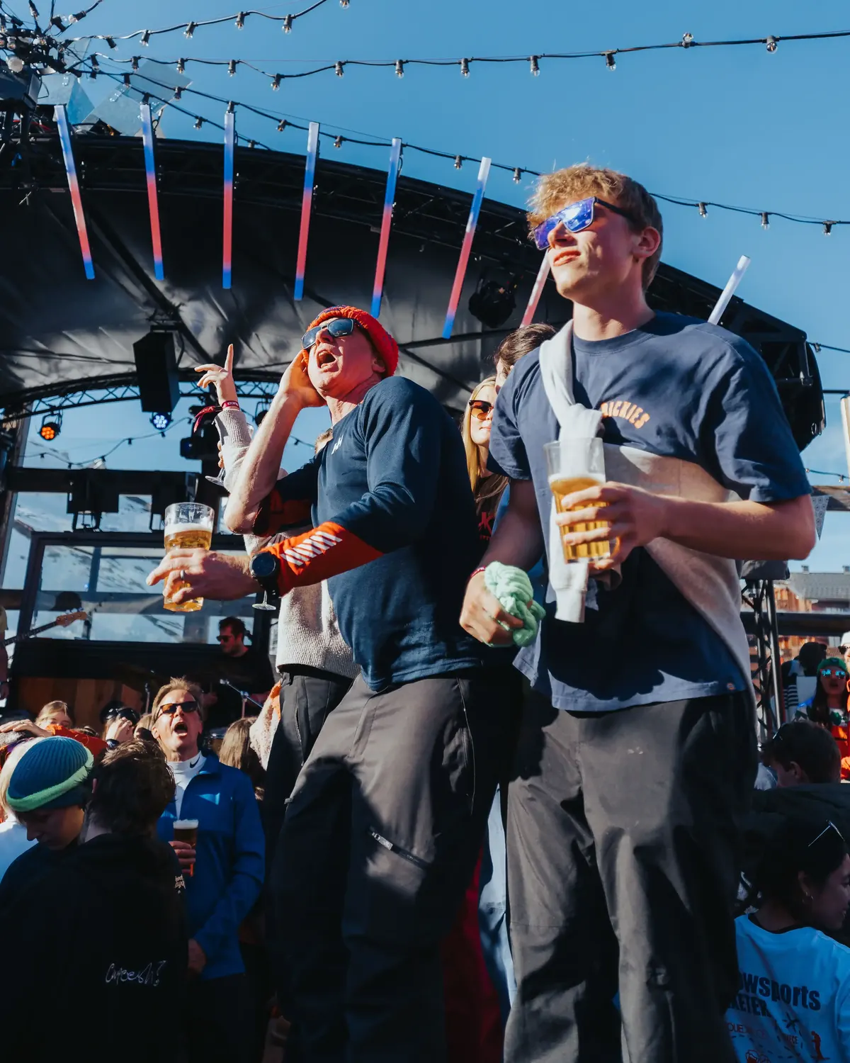 Members with drinks at an outdoor apres bar under strings of lights