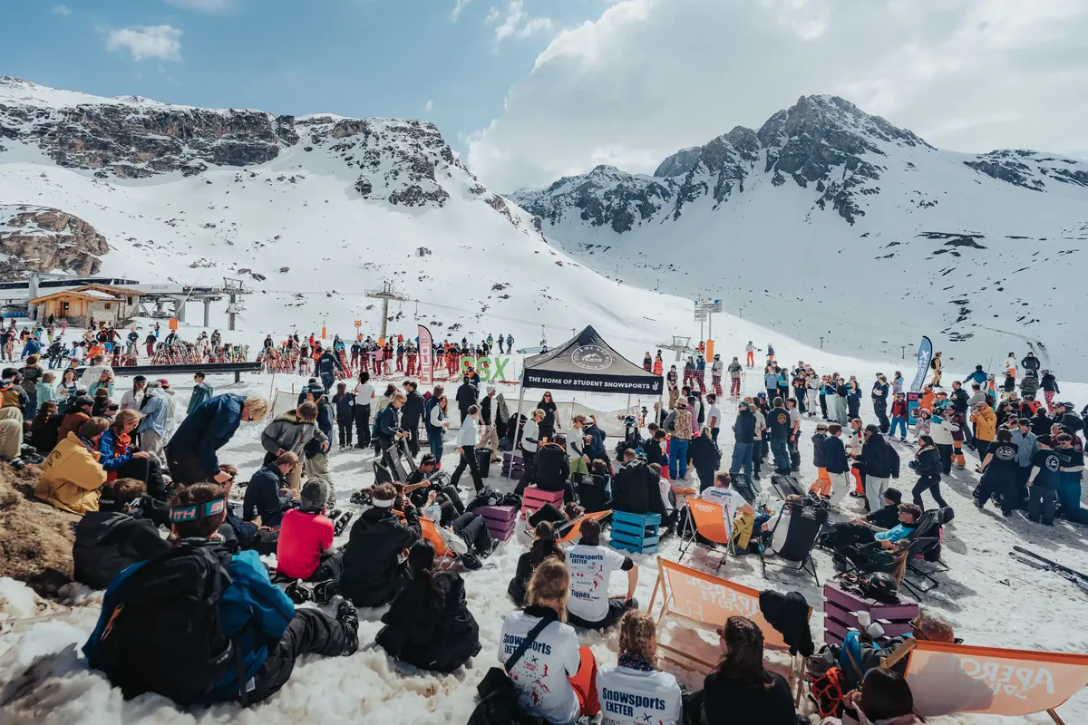 Crowd of students sitting out on the snow at a mountainside apres bar