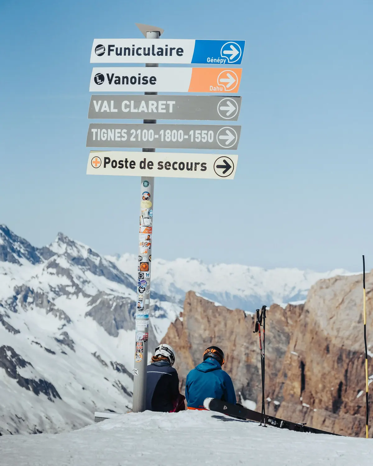 Piste signpost for Val Claret and Tignes with skiers resting beside it