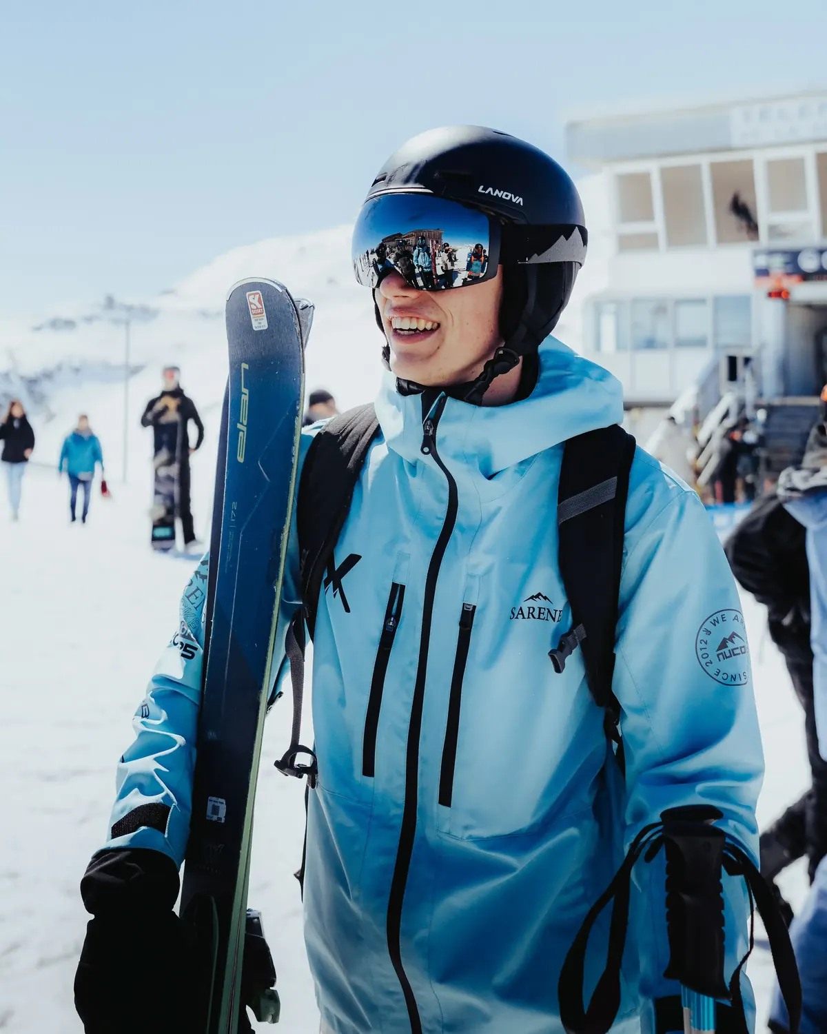 Member in an SSX jacket carrying skis at the lift base