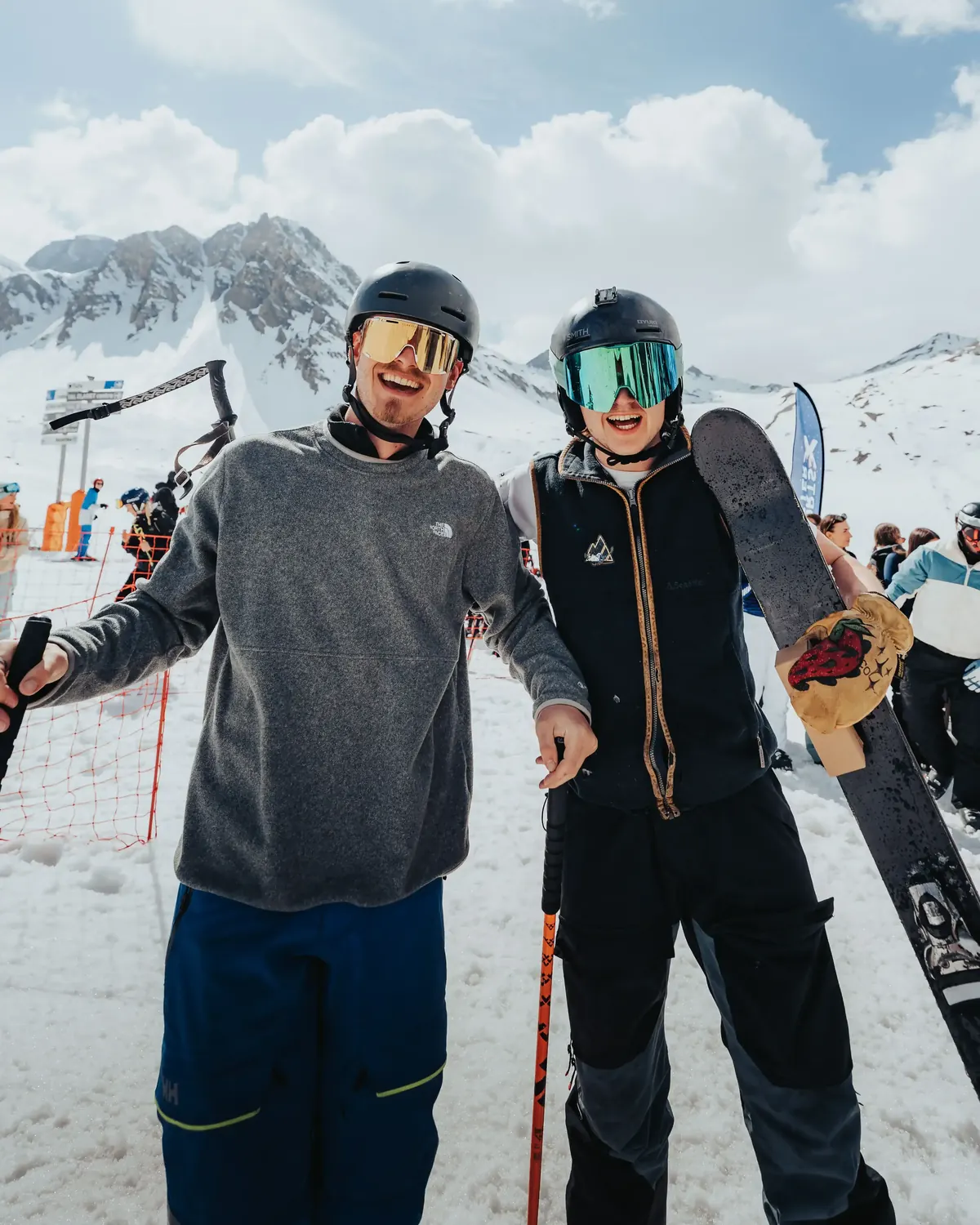 Two members posing with skis and boards at the bottom of a run