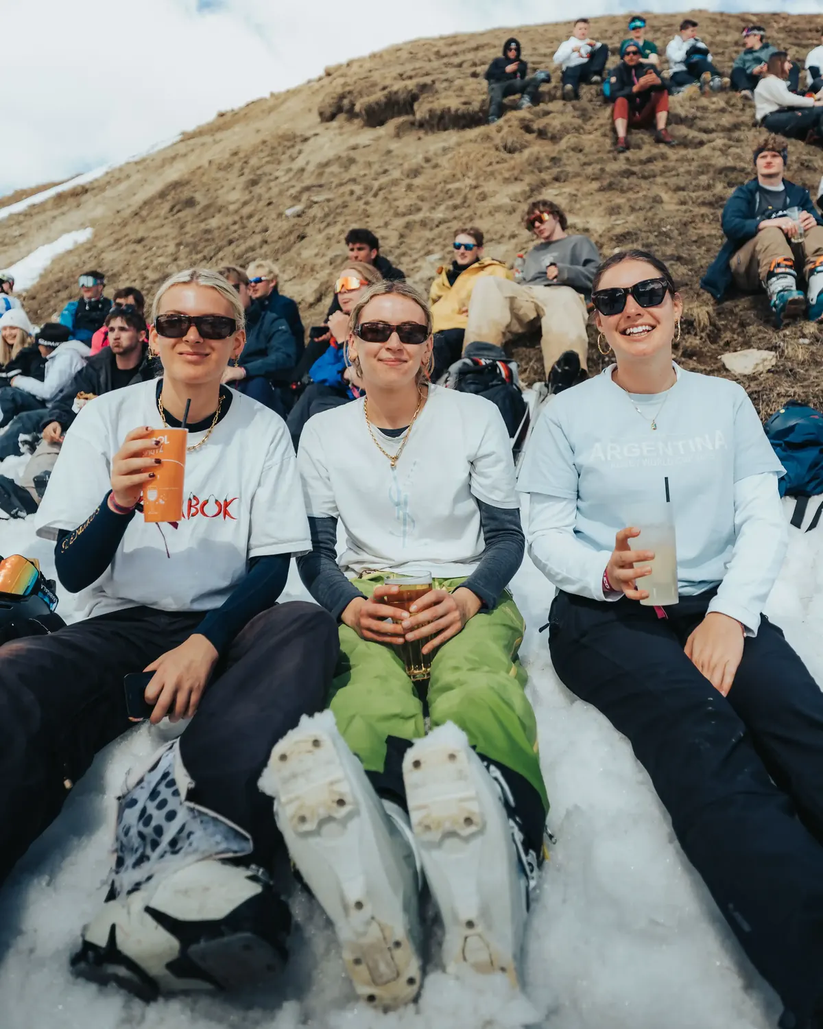 Three members sitting on the snow with drinks at an outdoor bar