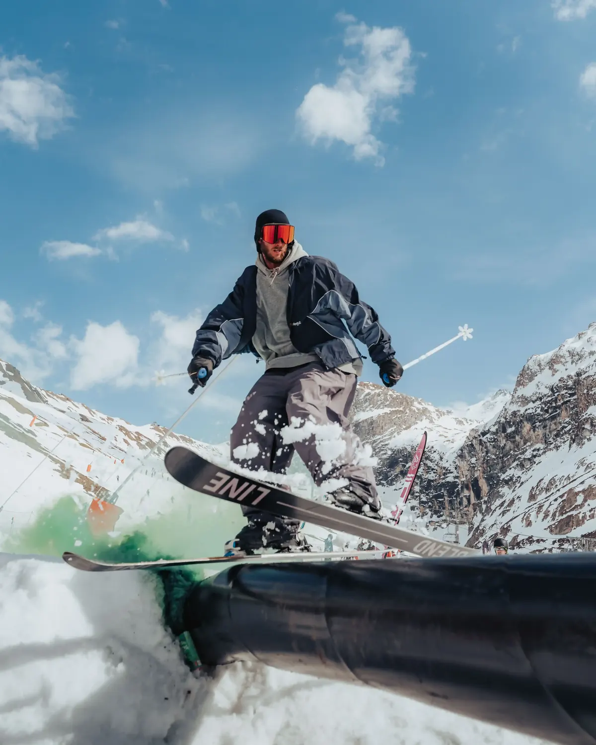 Skier pressing a rail in the snowpark with the mountains behind