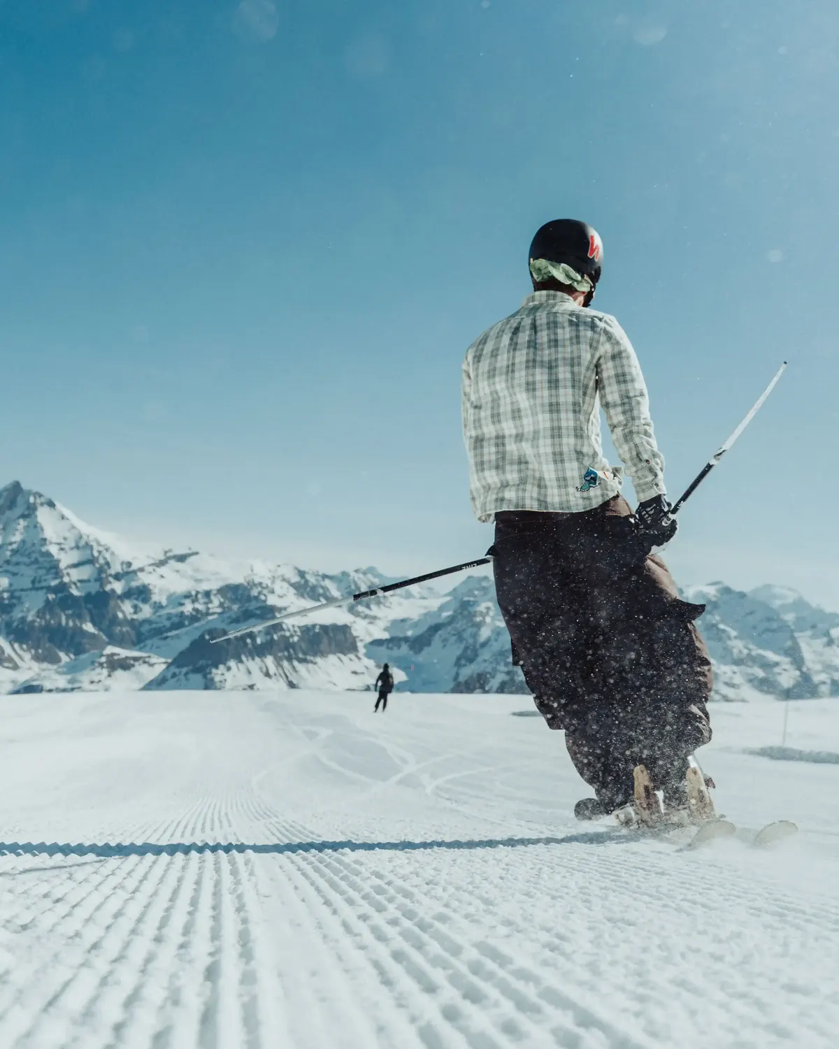 Skier in a checked jacket riding freshly groomed corduroy with the Alps behind