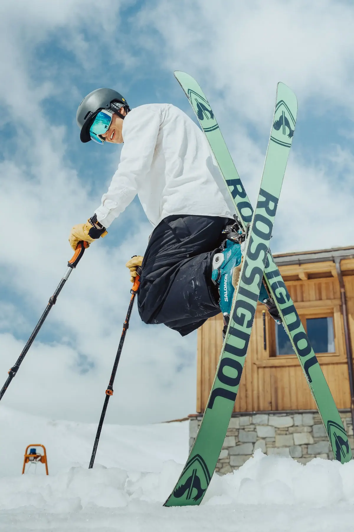 Skier grabbing their skis mid-jump beside a mountain chalet