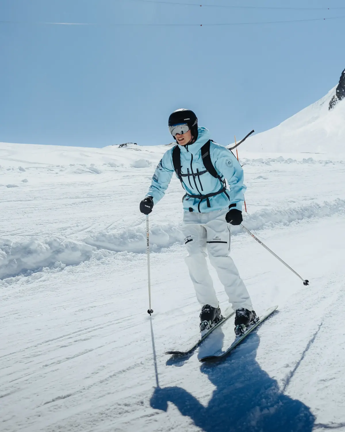 Skier in a pale blue jacket skiing towards the camera on a bluebird day