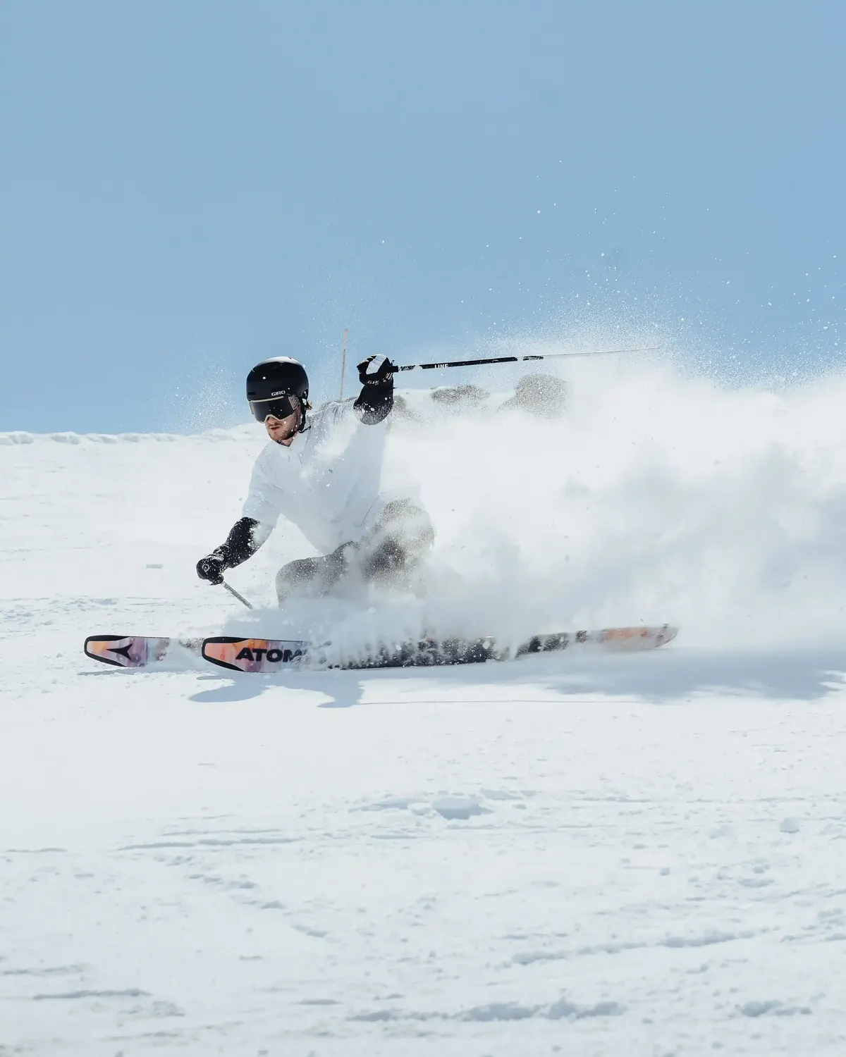 Skier carving hard and throwing up a wall of spray on a sunlit piste